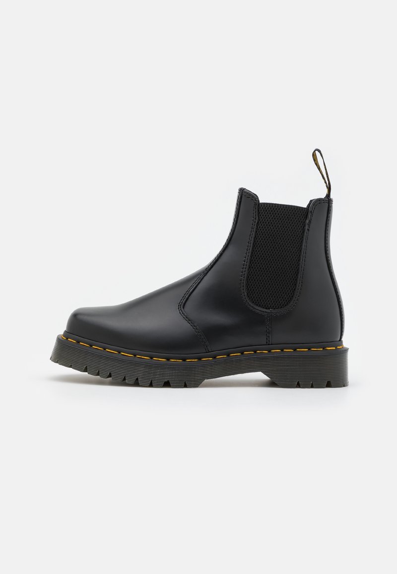 Bottine noire en cuir avec panneaux latéraux élastiques, surpiqûre jaune sur la semelle, languette au talon et semelle extérieure en caoutchouc texturée.