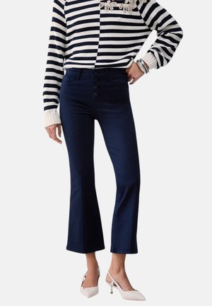 Donna che indossa jeans svasati a vita alta di colore blu navy, maglione a righe bianche e nere, braccialetti argentati e décolleté slingback bianchi con punta appuntita.