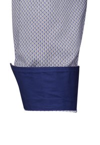 Tessuto blu e bianco con un design geometrico, caratterizzato da un polsino blu navy solido. Il polsino ha una consistenza liscia e cuciture ordinate.