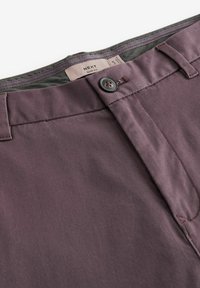 Slim-fit spodnie w bogatym burgundowym kolorze. Wykonane z gładkiego materiału, z zapięciem na guzik i kontrastującą podszewką w pasie.