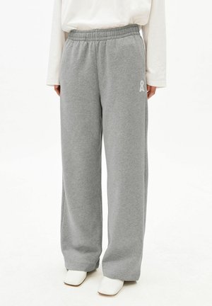 Personne portant un pantalon de survêtement gris ample avec une taille élastique et des bottines blanches à la cheville, associé à un haut blanc à manches longues.