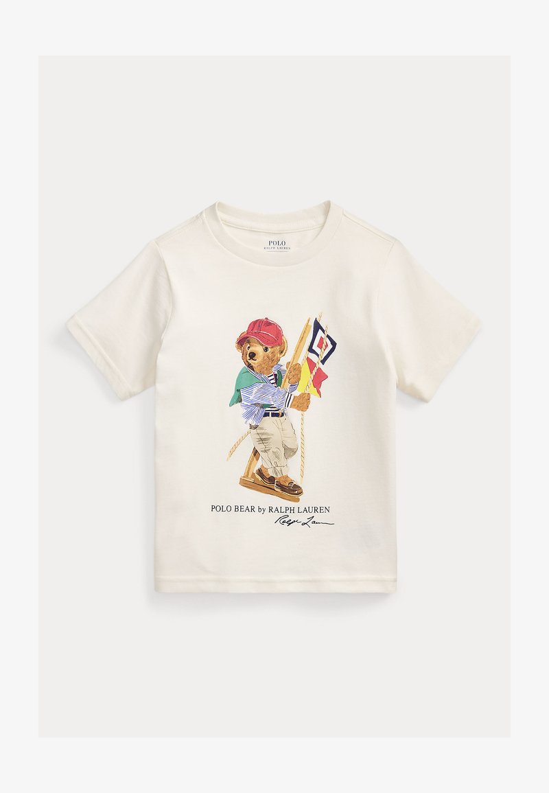 Λευκό t-shirt με κοντά μανίκια, με μικρή ζωγραφιά ενός αρκούδου που φοράει κόκκινο καπέλο και ριγέ πουκάμισο, κρατώντας ναυτικούς σημαίες σε μια ξύλινη κούνια.