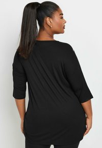 Mustatunika, jossa on kolmanneksen mittaiset hihat, rento leikkaus ja sileä pinta, ulottuu lantion alapuolelle ja siinä on yksinkertainen pääntie.