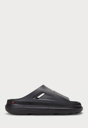 Melnas slēpšanas sandalītes ar gludu gumijas materiālu, kontūrveida formu, ventilācijas caurumiem un sarkanu akcentu uz papēža.