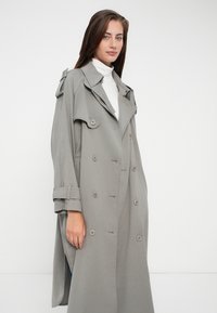Cappotto grigio con design doppiopetto, grandi bottoni, spalline e vestibilità rilassata. Tessuto morbido con una silhouette leggermente strutturata.