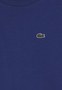 Granatowa bawełniana koszulka z okrągłym dekoltem i krótkimi rękawami. Posiada małe, haftowane zielone logo krokodyla na piersi.