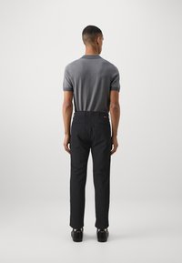 Polo grigio a maniche corte con motivo a zigzag, abbinato a pantaloni neri eleganti, che mostrano un design pulito e una vestibilità dritta.