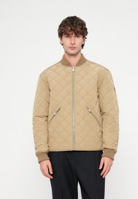 Béžová prešívaná bomber bunda so zipsovým zapínaním, rebrovanými manžetami a bočnými vreckami. Hladká textura s detailom v tvare diamantového vzoru.