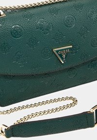 Groene leren handtas met een textuur en reliëfpatronen, goudkleurige hardware en een kettinghengsel. Heeft een frontale driehoekige logo-plaat.