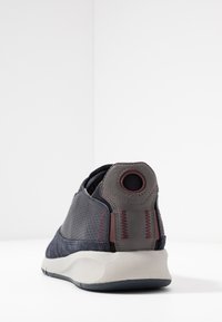 Scarpa sportiva navy e grigia con tessuto perforato, un tallone rotondo, cuciture a contrasto e una suola in gomma bianca.