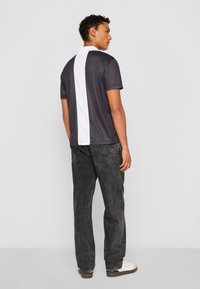 Grå polo t-shirt med en hvid vertikal stribe på ryggen, parret med sorte jeans og hvide sneakers. Glat stof med en tætsiddende pasform.