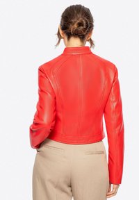 Veste cropped en cuir rouge avec des manches longues, des coutures détaillées et une texture lisse. Complétée par un pantalon beige.
