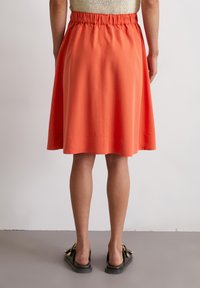 Bright orange knee-length skirt with an elastic waistband. Smooth texture and simple design, featuring a clean hem and no patterns.