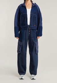 Laivastonsininen farkkutakki hupulla, isoilla etutaskuilla ja kontrastivärillä. Lörttifarkut laivastonsiniset, joissa on sivutaskut ja nappisulku.