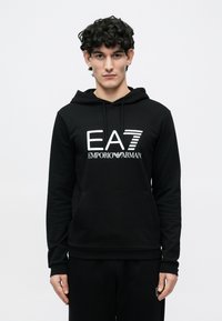 Fekete kapucnis pulóver, amelyen a elején nagy fehér "EA7 Emporio Armani" logó látható. Az anyag puhanak tűnik, enyhén laza szabással.