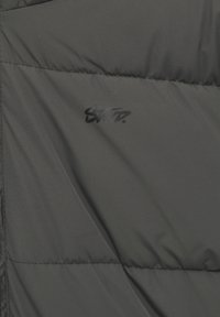 Tissu matelassé gris foncé avec de fines surpiqûres et un petit logo ou texte stylisé noir centré.