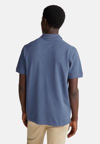 Koszulka polo w ciemnoniebieskim kolorze, krótki rękaw, kołnierzyk, wykonana z teksturowanej bawełny. Widok przedstawia tył, z prostym dołem.