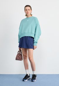 Sudadera oversized azul claro con logo blanco, falda mini a rayas marino, zapatillas negras, calcetines blancos y un bolso pequeño marrón.
