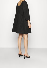 Svart, texturerad klänning med fyrkantig halsringning, puffärmar och utsvängd silhuett, kombinerad med svarta sandaler med öppen tå.