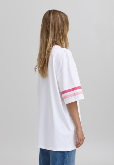Camiseta blanca de algodón con mangas cortas, presenta rayas rosas y rosa claro en las mangas. Corte holgado con un diseño casual.