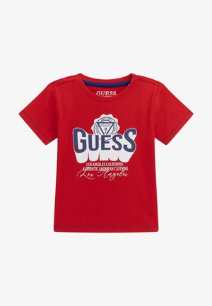 Red cotton short-sleeve t-shirt featuring large white and blue "GUESS" text with a circular logo and additional white text detailing.