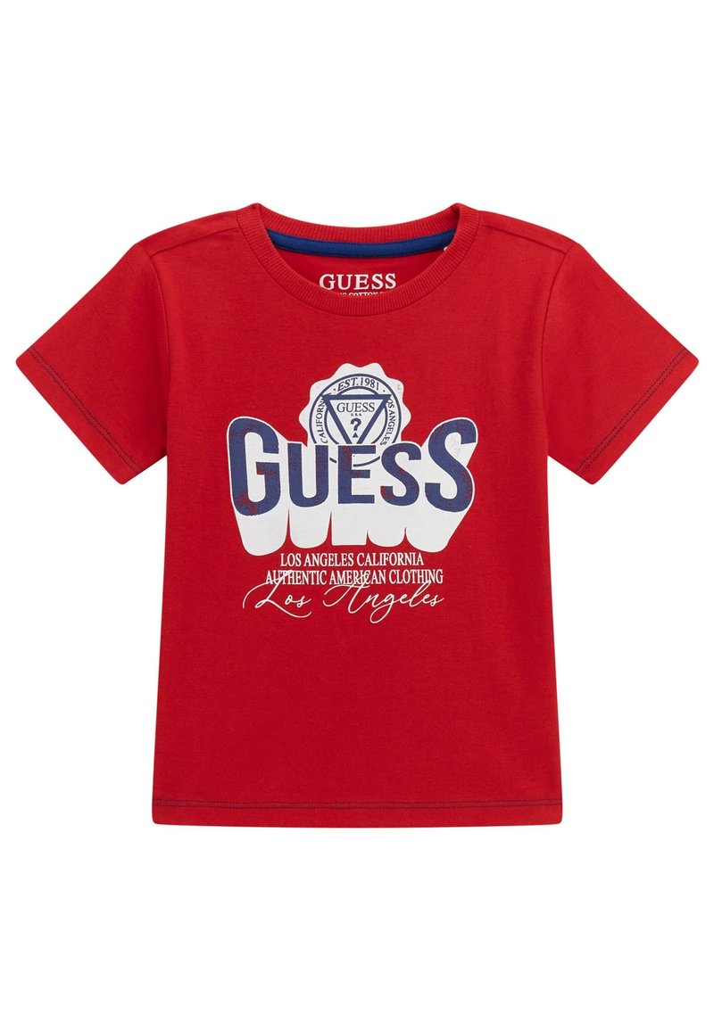 Rød bomulds t-shirt med korte ærmer, der har stor hvid og blå "GUESS" tekst med et cirkulært logo og yderligere hvid tekstbeskrivelse.