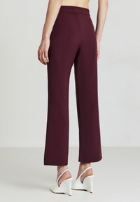 Pantaloni larghi bordeaux realizzati in tessuto morbido, con vita alta, tasche posteriori e abbinati a dei tacchi a cuneo bianchi.