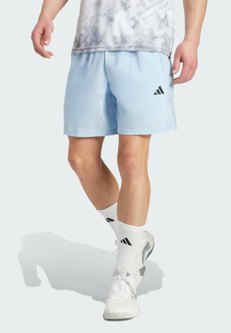 Svetlomodré športové šortky s hladkým povrchom, so čiernym logom Adidas. V páre s bielymi krátkymi ponožkami a šedými teniskami.