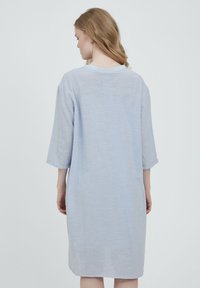Ljusblå linnéklänning med trekvartsl ånga ärmar, en lös passform och rund halsringning. Tyget har en subtil struktur.