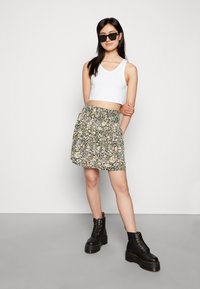 Saia com estampa floral e cintura franzida, top preto sem mangas e botas pretas robustas. A saia apresenta uma mistura de cores pasteis num fundo escuro.