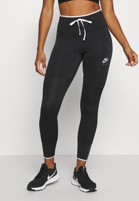 Czarne legginsy sportowe z wysokim stanem, białym sznurkiem, teksturowanymi panelami i logo Nike Air. W połączeniu z czarnymi butami sportowymi.