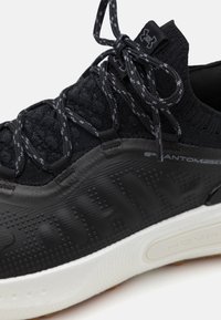 Black athletic shoe featuring a textured upper, sleek design, elastic laces, and a white midsole with a patterned black outsole.