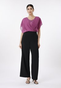 Lilla chiffon-topp med V-hals og dekorert design, kombinert med svarte vide bukser. Inkluderer svarte hæler med stropper og sølvfargede tilbehør.