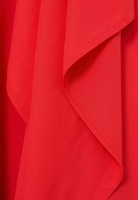 Punane kangas pehme langevusega ja nähtavate õmblustega servadel, moodustades õrnad voldid.