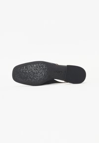Černá bota s hladkým povrchem, která má výřezový design a vzorovanou texturovanou podrážku. Minimální kovové prvky a štíhlý tvar.