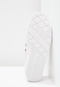 Vit gummisula på sneakers med ett strukturerat, zigzag-mönster och "Calvin Klein Jeans" präglat. Ljus persikofärgad överdel syns på sidan.