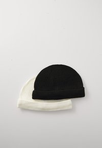 To ribbet strikkede beanies, en sort og en hvid, stablet med en rullet kantdetalje nederst på hver hat.