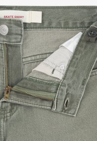 Πράσινα σορτς από τζιν για σκέιτ, με φερμουάρ, κουμπί κλεισίματος και μία μικρή τσέπη για κέρματα. Το ύφασμα έχει διακριτική υφή και ραφές με λεπτομέρειες.