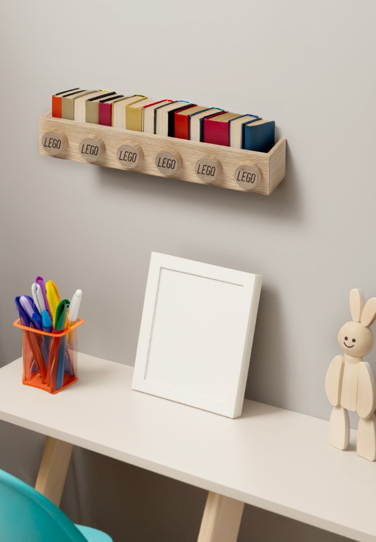 Houten plank met vijf gestapelde LEGO-boeken in verschillende kleuren. Daaronder een oranje pennenhouder, een wit fotolijstje en een houten figuurtje met een ronde kop.