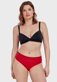 Crni bikini s uvijenim prednjim dijelom i podešivim naramenicama, uparen s visokim crvenim bikini gaćicama. Glatka tkanina, minimalistički dizajn.