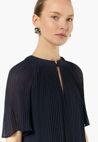 Granatowa plisowana sukienka z krótkimi, zwiewnymi rękawami i detalem w kształcie dziurki w dekolcie. Gładki materiał o miękkiej fakturze i subtelnym połysku.