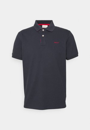 Tengerészkék pamut póló, lapos kötésű gallérral, kétsoros gombolással és piros hímzett logóval a mellrészen.