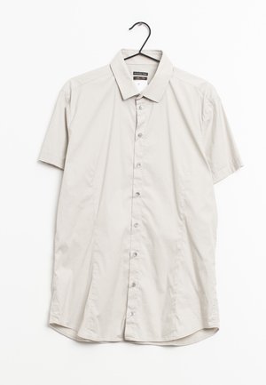 Camisa de manga corta de color gris claro, hecha de tela suave, con cuello puntiagudo y botones al frente, colgando de un gancho negro.