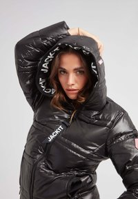 Svart pufferjacka med blank yta, huva med logofoder och dragkedjefickor. Har en quiltad design och varumärkesmärke.