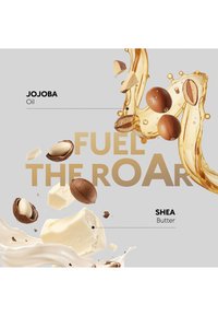 Ingrédients d’huile de jojoba et de beurre de karité montrés avec des noix, des morceaux crémeux et des éclaboussures d’huile dorée sur un fond gris clair avec le texte « Fuel the Roar ».