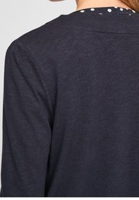 Marinblå tröja med texturerad yta, med rund halsringning prydd med ett prickmönster längs insidan av ryggen.