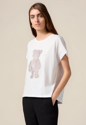 T-shirt en coton blanc avec une coupe décontractée, présentant un design de ours texturé composé de strass brillants sur le devant.