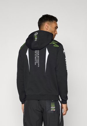 Black hooded sweatshirt featuring white accents, vibrant green details, and printed text on the back. Smooth fabric with a relaxed fit.