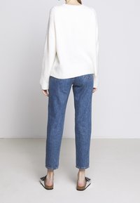 Kremowy sweter z dzianiny o prążkowanej strukturze, zestawiony z jasnoniebieskimi, prostymi jeansami i czarnymi sandałami z kokardkami.