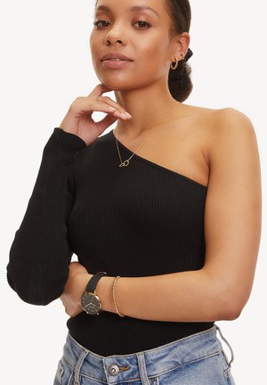 Schwarzes, geripptes Top mit einem Schulterträger und langem Ärmel, kombiniert mit einer zarten, goldenen Halskette und einer schwarzen Uhr, getragen mit hochtaillierten Jeans.